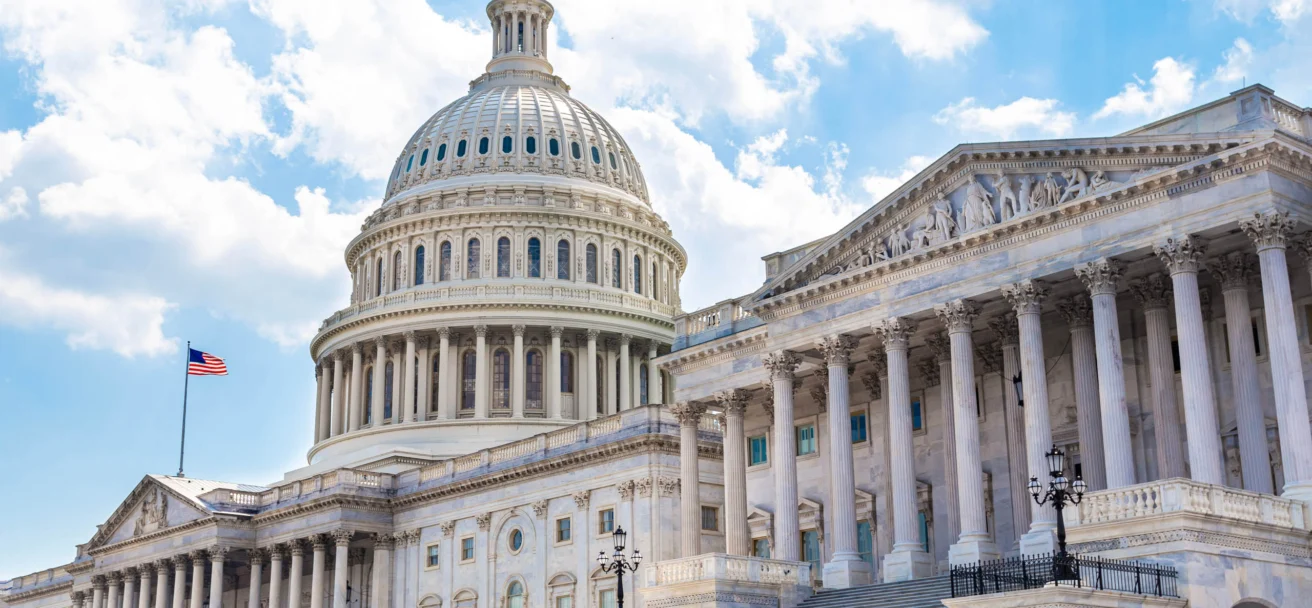 Exterior view of the U.S. Capitol building in Washington, D.C., featuring its iconic dome, columns, and steps under a partly cloudy sky.